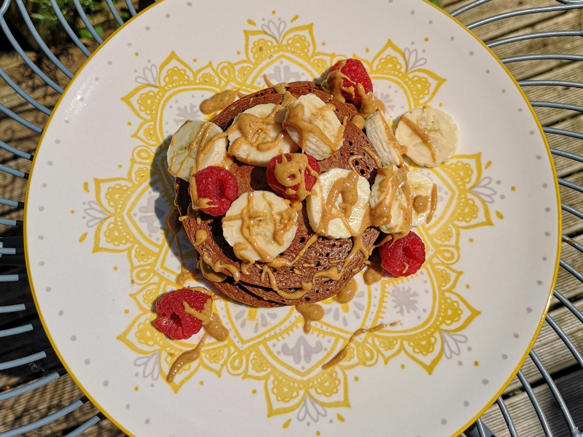 Aerial view of pancakes on plate with raspberries and bananas.